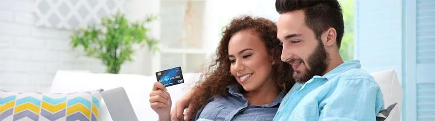 couple on couch with blue credit card and laptop