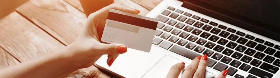 woman's hand with red nails holding a white credit card on top of a laptop