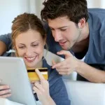 Excited couple watching their tablet holding a credit card