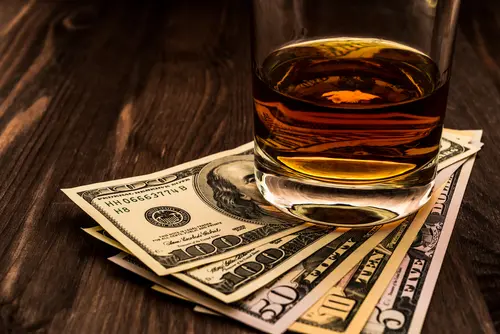 glass of whisky sitting on stack of dollar bills