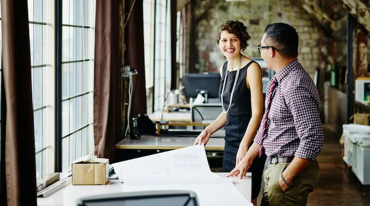 Smiling female architect leading project discussion with coworkers at workstation in office