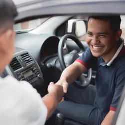 Man shaking hands with a car salesman at a dealershipA young man smiling in a car