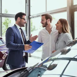 Young couple talking with car salesman inside a car dealership