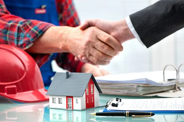 Close-up of construction worker and business man shaking hands with model house on desk