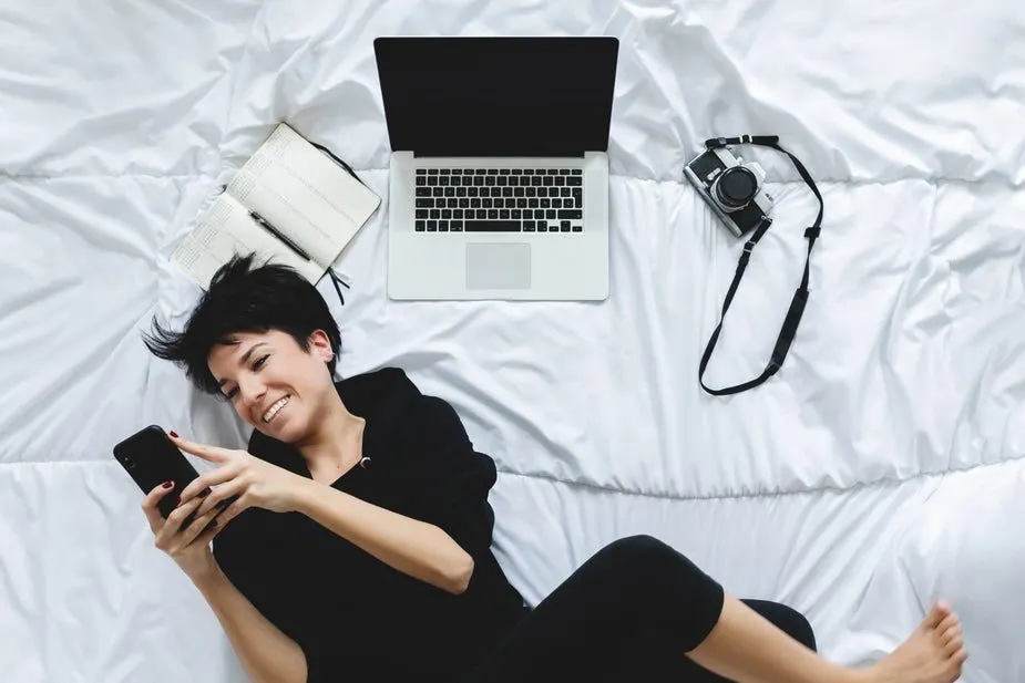 Woman blogger lying on duvet with laptop, camera and phone